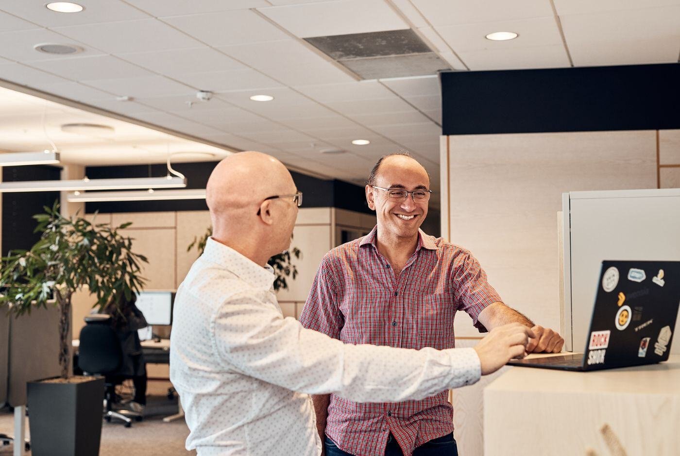 Two male colleagues smiling while looking at a computer screen